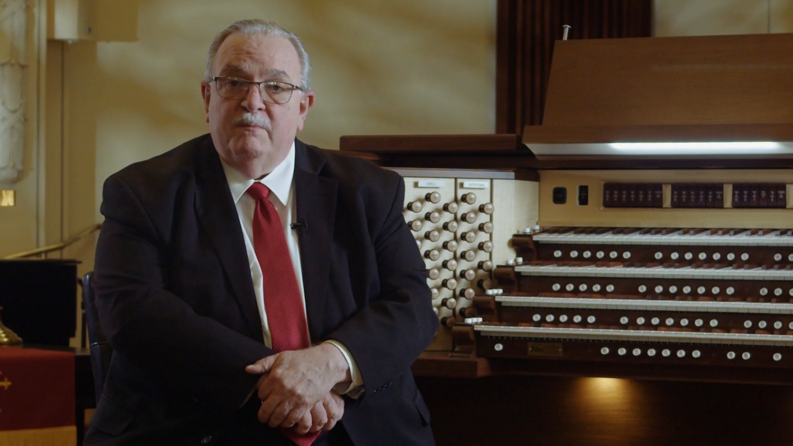Arvin Starrett seated beside the Allen organ at First United Methodist Church, Paris